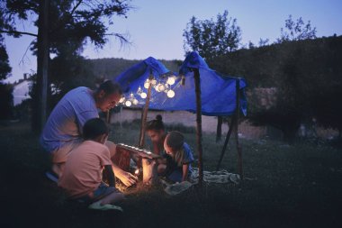 Baba ve çocuklar arka bahçedeki çadırın altında oynuyorlar..
