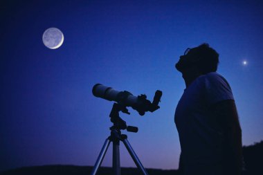Teleskopla Ay 'ı ve yıldızları izleyen bir astronom. Benim...