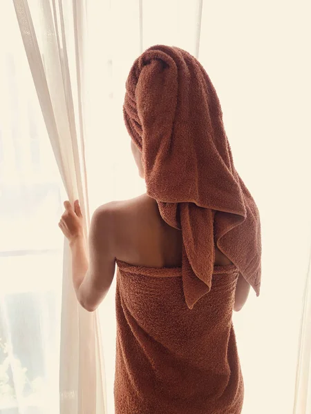 Femme avec serviette devant une fenêtre et un rideau . — Photo