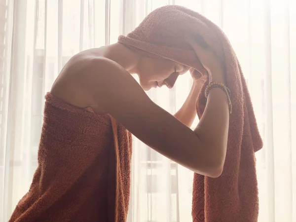 Vrouw met handdoek voor een raam en gordijn. — Stockfoto
