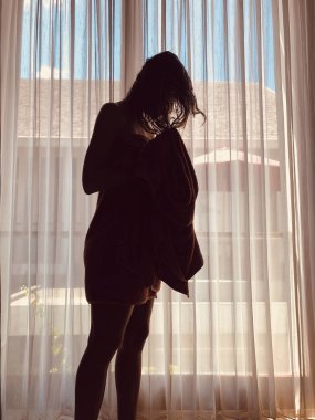 Pencerenin önünde ve perdede havlusu olan kadın..