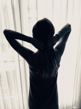 Pencerenin önünde ve perdede havlusu olan kadın..