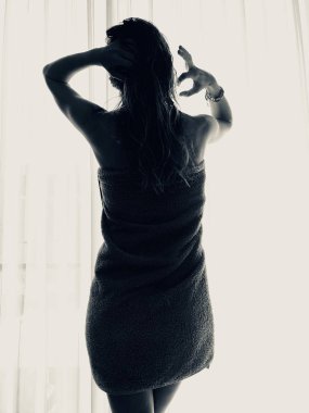 Pencerenin önünde ve perdede havlusu olan kadın..