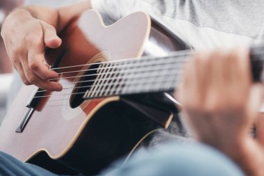 Adam oturma odasında akustik gitar çalıyor..