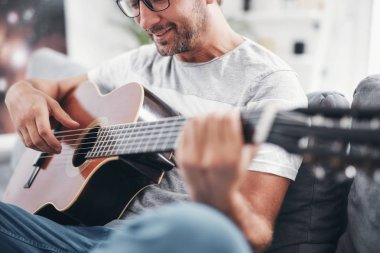 Adam oturma odasında akustik gitar çalıyor..