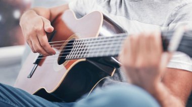 Adam oturma odasında akustik gitar çalıyor..