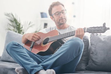 Adam oturma odasında akustik gitar çalıyor..
