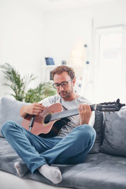Adam oturma odasında akustik gitar çalıyor..