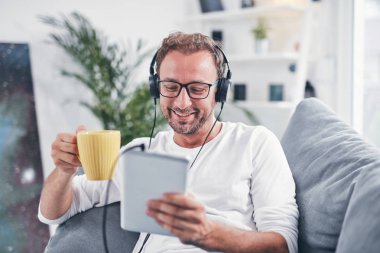 Adam müzik dinliyor ve oturma odasında tablet kullanıyor..