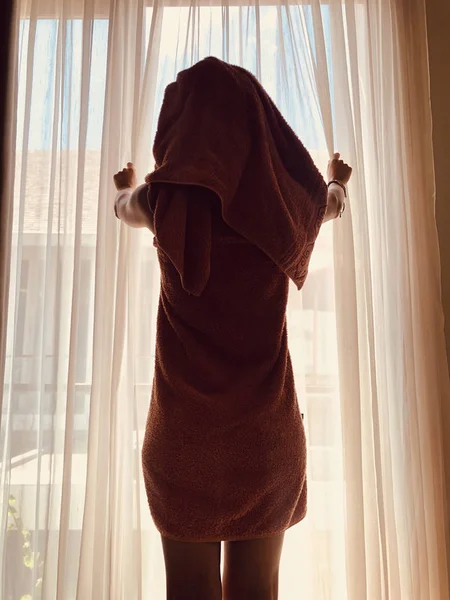 Kobieta z ręcznikiem przed oknem i zasłoną. — Zdjęcie stockowe