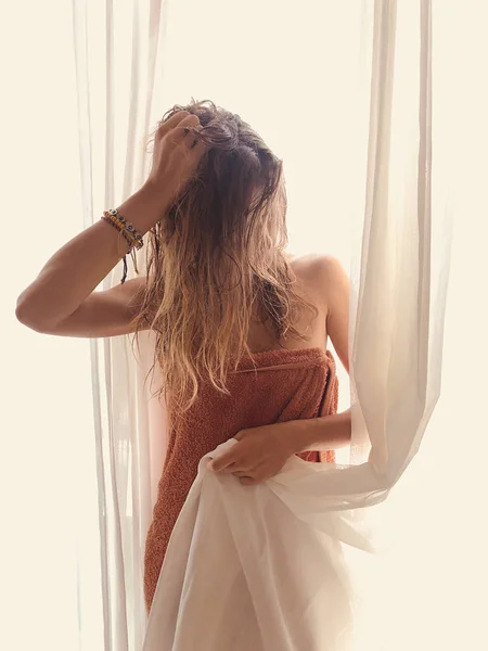 Femme avec serviette devant une fenêtre et un rideau . — Photo
