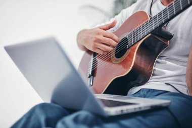 Adam oturma odasında akustik gitar çalıyor..