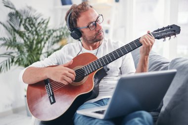 Adam oturma odasında akustik gitar çalıyor..