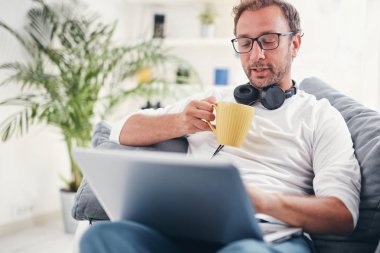 Adam müzik dinleme ve oturma odasında dizüstü bilgisayar kullanma.