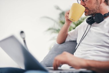 Adam müzik dinleme ve oturma odasında dizüstü bilgisayar kullanma.