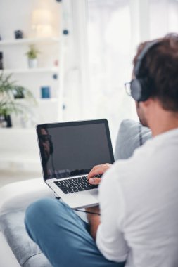 Adam müzik dinleme ve oturma odasında dizüstü bilgisayar kullanma.