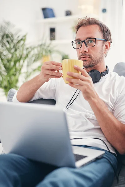Hombre escuchando música y utilizando el ordenador portátil en la sala de estar . — Foto de Stock
