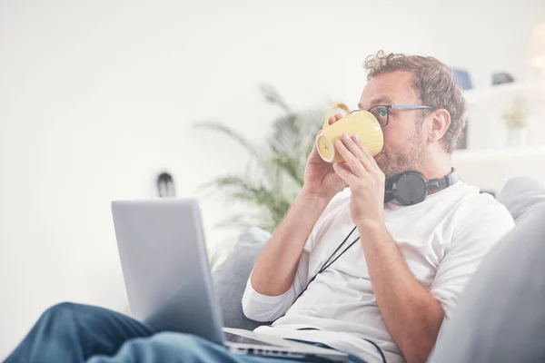 Hombre escuchando música y utilizando el ordenador portátil en la sala de estar . — Foto de Stock