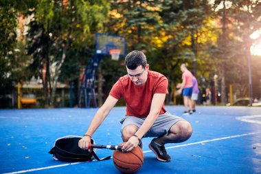 Basketbol topunu şehir merkezinde elle pompalayan bir adam.