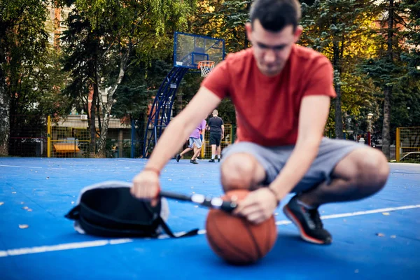 Ο άνθρωπος φουσκώνει μπάλα του μπάσκετ με μια αντλία χέρι στην αστική cour — Φωτογραφία Αρχείου