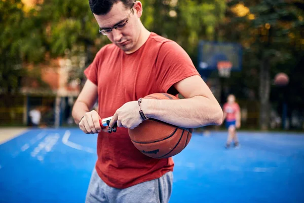 Uomo gonfiare pallone da basket con una pompa a mano sul cour urbano — Foto Stock