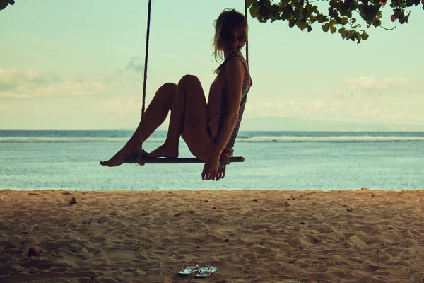 Young woman swinging on a sandy tropical beach.