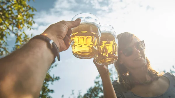 Pareja sosteniendo vasos de cerveza en el aire desde el punto de vista personal — Foto de Stock