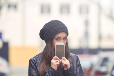 Soğuk mevsimde şapkalı genç bir kadın cep telefonu tutuyor.