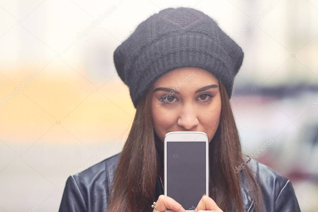 Young woman with hat holding cellphone in cold season on the str