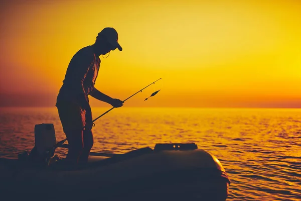 Sylwetka rybaka łowiącego ryby o zachodzie słońca na otwartym morzu — Zdjęcie stockowe