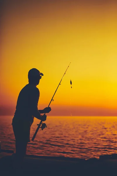 Silhouet van een visser die in zonsondergang vist op open zee — Stockfoto