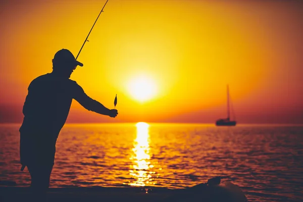 Silhouet van een visser die in zonsondergang vist op open zee — Stockfoto