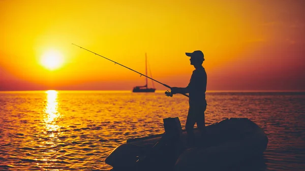 Silhueta de um pescador pescando em tempo de pôr do sol no mar aberto — Fotografia de Stock