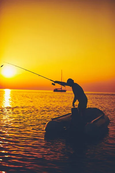 Silhueta de um pescador pescando em tempo de pôr do sol no mar aberto — Fotografia de Stock