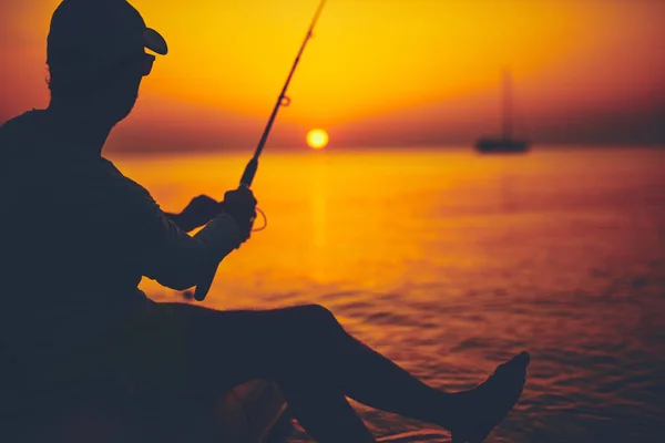 Silhueta de um pescador pescando em tempo de pôr do sol no mar aberto — Fotografia de Stock