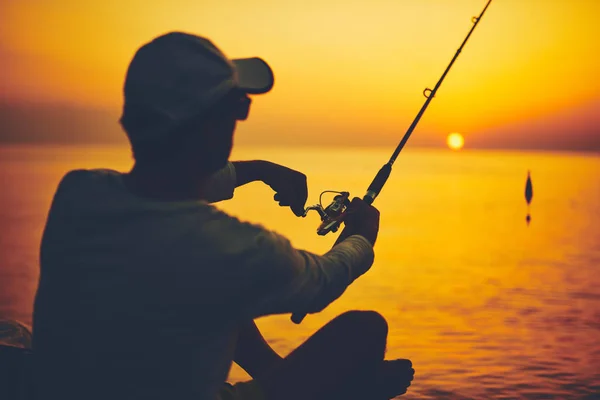 Silhouet van een visser die in zonsondergang vist op open zee — Stockfoto