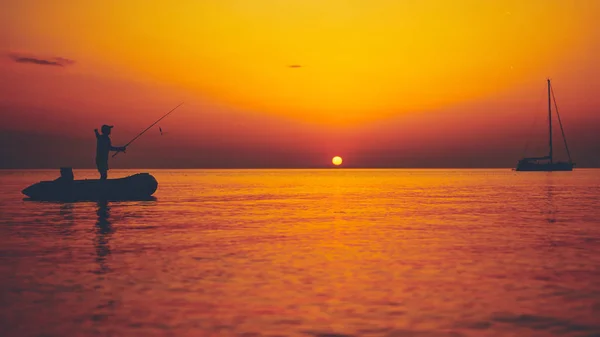 Silueta de un pescador pescando al atardecer en mar abierto — Foto de Stock