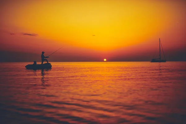 Silueta de un pescador pescando al atardecer en mar abierto — Foto de Stock