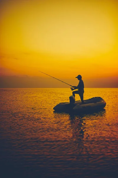 Silhueta de um pescador pescando em tempo de pôr do sol no mar aberto — Fotografia de Stock