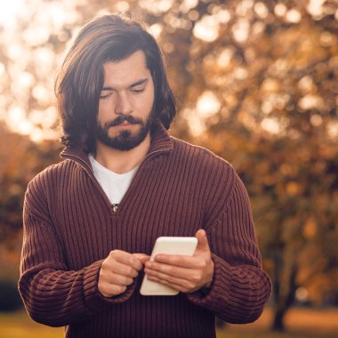 Sonbahar parkında cep telefonu kullanan modern bir adam..