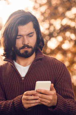 Sonbahar parkında cep telefonu kullanan modern bir adam..