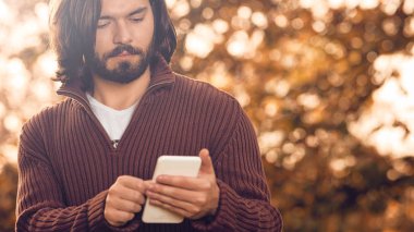 Sonbahar parkında cep telefonu kullanan modern bir adam..