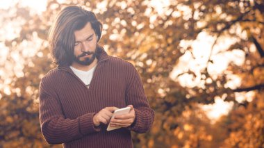 Sonbahar parkında cep telefonu kullanan modern bir adam..