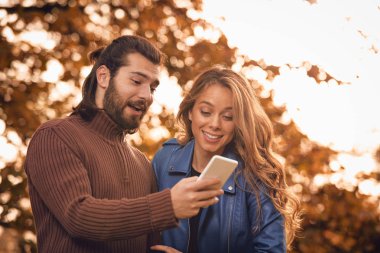 Genç çift sonbahar renkli park'cep telefonu kullanma.