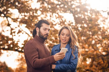 Genç çift sonbahar renkli park'cep telefonu kullanma.
