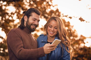Genç çift sonbahar renkli park'cep telefonu kullanma.
