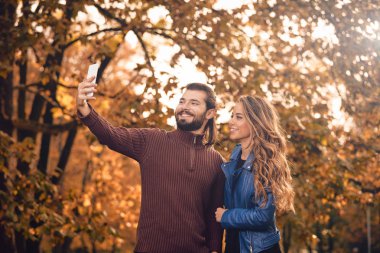 Genç çift sonbahar renkli park'cep telefonu kullanma.