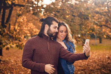 Genç çift sonbahar renkli park'cep telefonu kullanma.