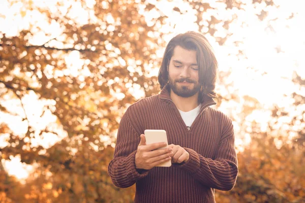 Hombre moderno usando el teléfono celular en el parque de color de otoño . —  Fotos de Stock