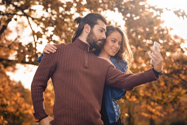 Jeune couple utilisant un téléphone portable en automne parc coloré . — Photo